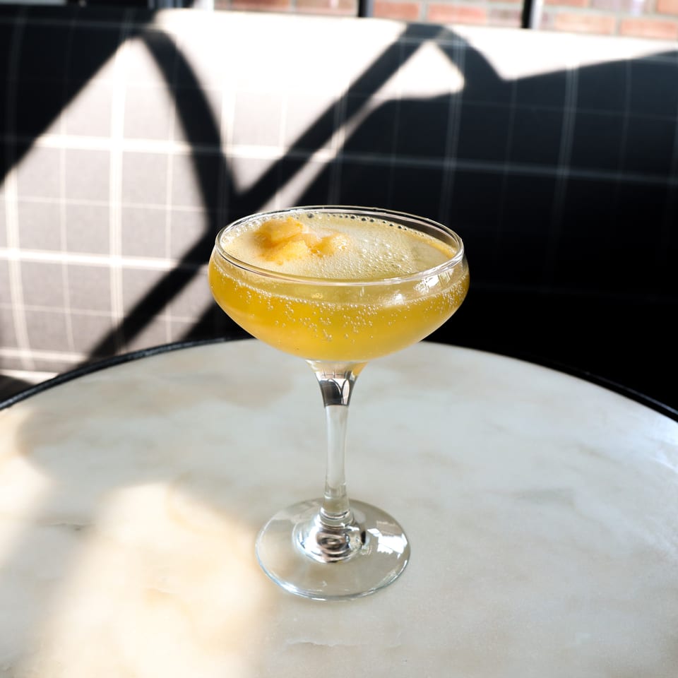 Golden, frothy cocktail with citrus garnish served in a coupe glass on a marble table.